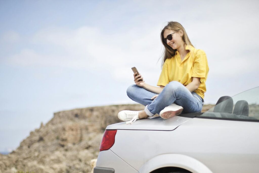 Ragazza seduta su un cofano di un'auto - prestiti.com